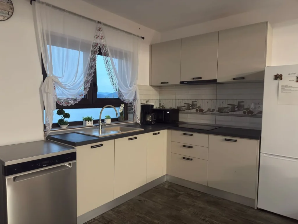 Bucătăria cabanei, cu mobilier alb, plită și blat de lucru
