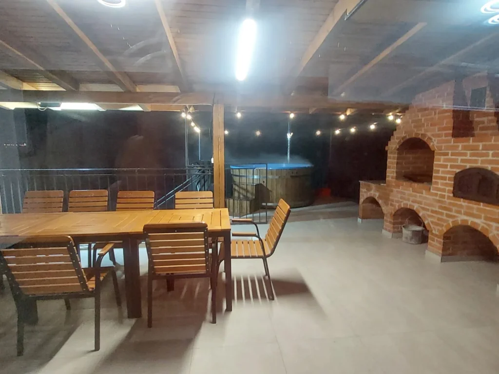 Terasa acoperită cu masă din lemn, grătar din cărămidă și lumini de seară